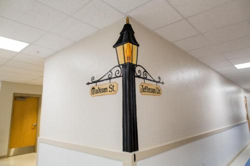 Closeup of a lamp post with street signs painted on the corner of a school hallway