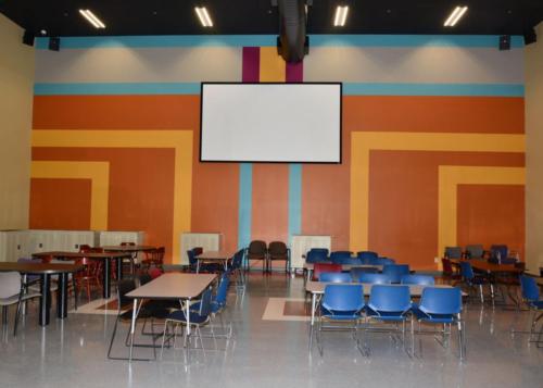 A large group room with tables and a projector screen