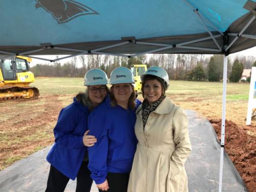 Three women standing beneath a canopy tent at the school groundbreaking