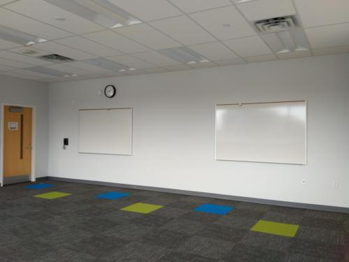 An unfurnished room with two whiteboards on the wall