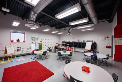 Classroom with circular tables and red rugs and cabinets