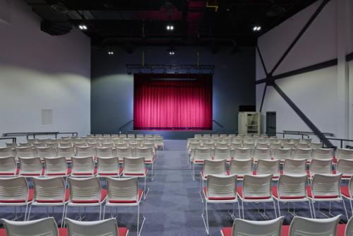 An auditorium lined with chairs in front of a large red curtain