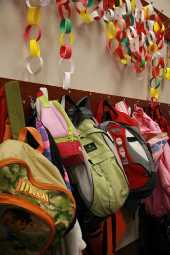 A closeup of student backpacks hanging from a classroom wall