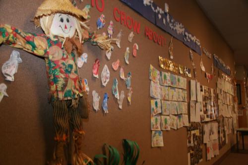 A classroom wall decorated with a scarecrow and student art
