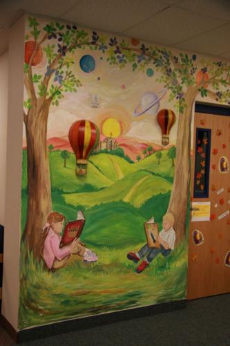 A mural of children reading underneath trees with hot air balloons in the background